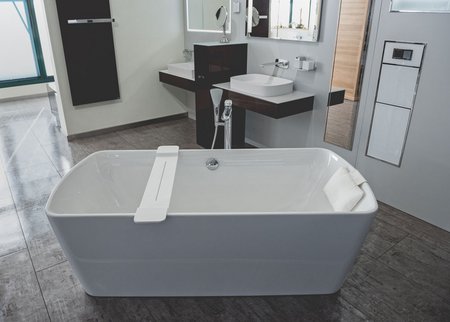 Freistehende Badewanne mit Kopfstütze, daneben Waschtisch und großer Spiegel in einer modernen Badausstellung.