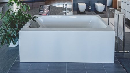 Quadratische, freistehende Badewanne in einer modernen Ausstellung, umgeben von Sanitärkeramik und Pflanzen.