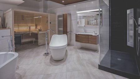 Weitläufige Badausstellung mit freistehender Badewanne, Glasdusche, integrierter Sauna und modernem Waschtisch.